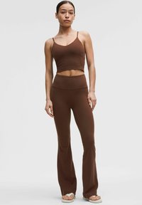 Braunes, kurzes Tanktop und weit ausgestellte Leggings aus einem weichen, glatten Stoff. Das Set verfügt über dünne Träger und ein hochgeschnittenes Design.