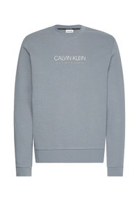 Felpa grigia realizzata in materiale morbido, con collo rotondo e polsini a coste. Logo "CALVIN KLEIN" visibile sul fronte.