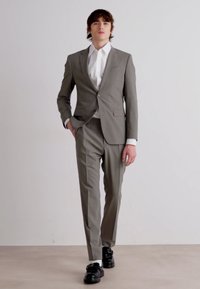 Completo grigio chiaro con vestibilità slim, giacca a un bottone e pantaloni coordinati. Abbinato a una camicia bianca e scarpe nere. Texture liscia.