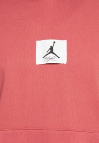 Sudadera roja con una tela texturizada que presenta una etiqueta blanca y el logo negro "Jumpman" con la palabra "Flight" debajo.