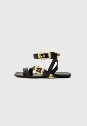 Sandales en cuir noir avec des accents de boucles dorées, présentant plusieurs brides et un design de semelle plate pour un port ouvert.