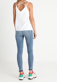 Bílý bezramenný top s křížovými popruhy, zkombinovaný s modrými úzkými džíny. Vhodné sportovní tenisky s barevnými akcenty na podrážkách.