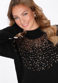 Maglione nero con colletto alto, decorato con paillettes oro rosa principalmente sul petto, dotato di maniche lunghe e una texture morbida.