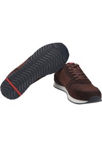 Scarpe sportive marroni che presentano una combinazione di pelle liscia e suede testurizzato. La suola ha un motivo a zigzag con un accento rosso.