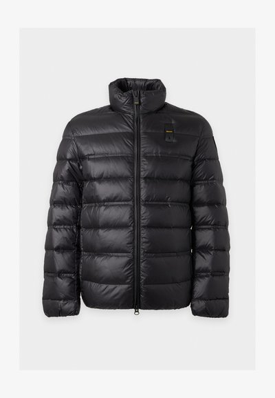 Veste d'hiver noire matelassée avec quilting horizontal, col montant, fermeture éclair à l'avant et un petit logo jaune et noir sur la poitrine.