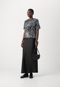 Haut à manches courtes en sequins noirs associé à une longue jupe en satin noir. La tenue est complétée par un petit sac à main noir et des mocassins élégants.