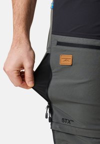 Pantalons d'extérieur gris avec une poche zippée et une étiquette tissée. Le matériau semble durable et léger, avec un insert noir contrastant.