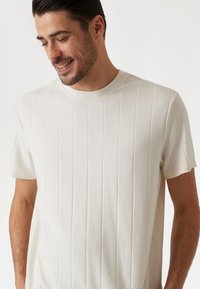 Hellbeige gerippte Strick-T-Shirt mit kurzen Ärmeln und Rundhalsausschnitt, mit subtiler Textur und vertikalen Linienmustern.