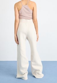 Světle růžový žebrovaný top s ramínky v kombinaci s širokými volnými kalhotami z měkké látky v barvě off-white, které mají vysoký pas a volný střih.