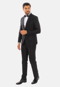 Tuxedo nero con revers in satin, camicia bianca e papillon nero. Design slim fit con scarpe eleganti nere lucide, tessuto morbido e silhouette sartoriale.