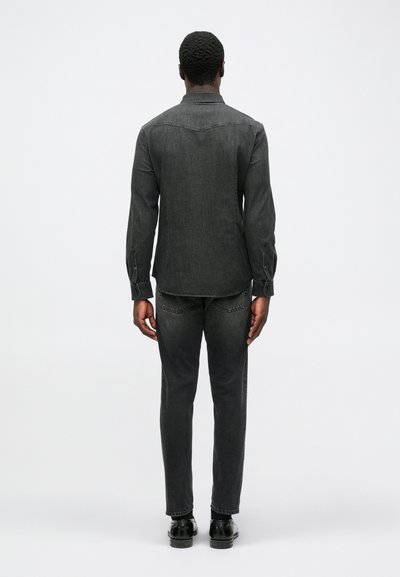 Dark gray denim shirt with a spread collar, buttoned cuffs, and a slightly curved hem, paired with matching gray jeans and black shoes.