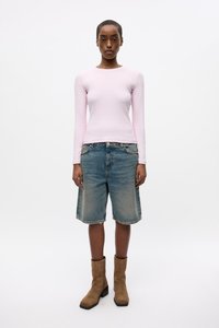 Maglia a maniche lunghe rosa chiaro, pantaloni corti in denim sbiadito con orlo sfrangiato e stivaletti color camoscio con punta quadrata e dettaglio con zip.