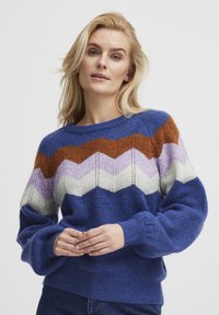 Gebreide trui met een blauwe basis, voorzien van een zigzagpatroon in oranje, lavendel, crème en donkerder blauw. Lange mouwen en gemêleerd stof.