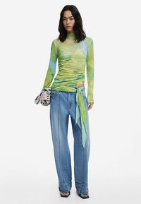 Hosszú ujjú, zöld és kék batikolt felső világos színű, bő szárú farmerral, amelyet kötött részletek díszítenek. Az összeállításhoz mintás borítéktáska tartozik.