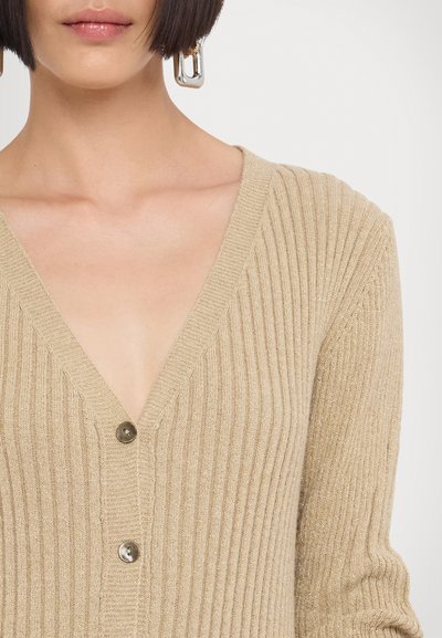 Beige geribbelde cardigan met een V-hals, voorzien van een knoopsluiting en een gestructureerde afwerking. Geaccentueerd met een subtiele metallic glans.