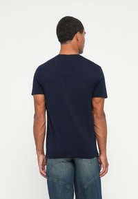 Camiseta de algodón azul marino con cuello redondo, mangas cortas y corte recto, exhibida desde la parte posterior en un fondo neutral.