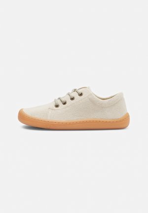 Lysebeige canvas lav høj sneaker med fire metaløjer, beige snørebånd og en tyk tan farvet gummisål, vist i højre sideprofil.
