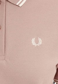 Polo shirt in rosa tenue con un tessuto texture, caratterizzata da un colletto bianco con righe e un logo alloro ricamato di colore bianco sul petto.