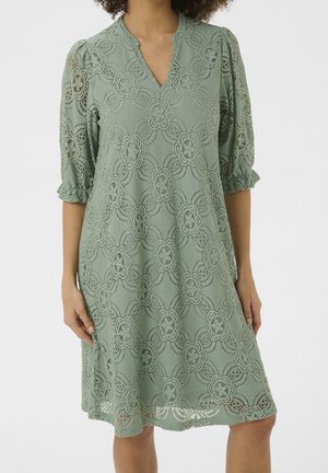 Robe en dentelle verte avec un col en V, des manches bouffantes, des motifs floraux complexes et une silhouette décontractée, arrivant à mi-cuisse.
