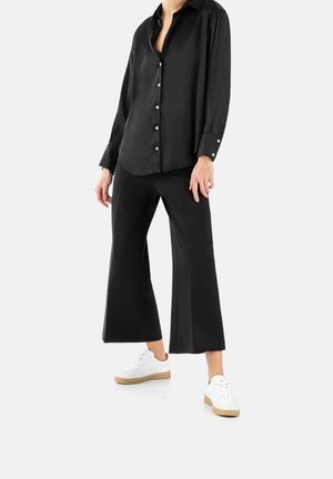 Black, long-sleeve satin shirt with buttons, paired with wide-leg black trousers and white sneakers featuring a beige sole.