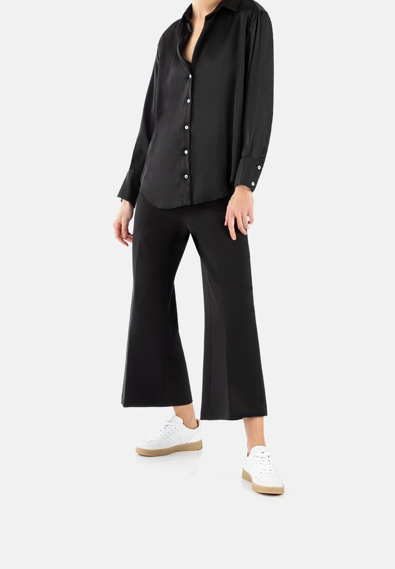 Camicia in satin nera a maniche lunghe con bottoni, abbinata a pantaloni neri a gamba larga e sneakers bianche con suola beige.