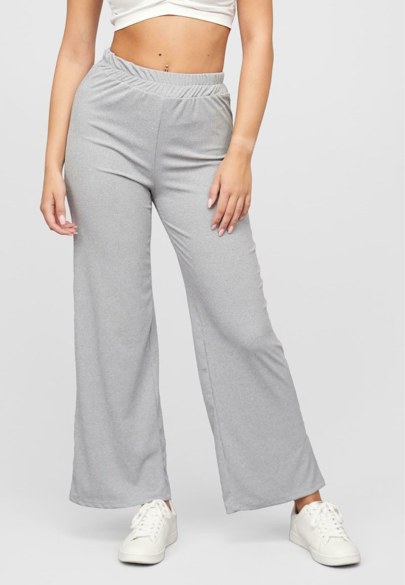Pantalons de lounge larges gris clair en tissu doux avec une taille élastique. Associés à des baskets blanches pour un look décontracté.