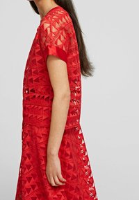 Vestido rojo con recortes triangulares y un diseño en capas. Mangas cortas, escote redondo y tejido texturizado.