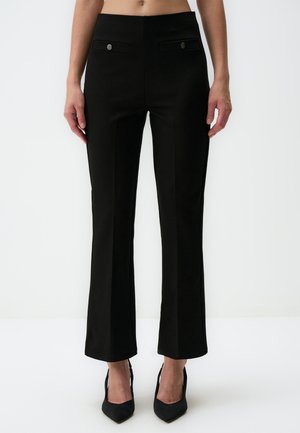 Black, fitted pants with front pockets and metal buttons; smooth texture, slightly flared at the hem, paired with black high-heeled shoes.