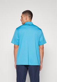 Polo de culoare albastră deschisă, cu un model de puncte negre mici, mâneci scurte și guler. Prezintă logo-ul Under Armour pe spate.