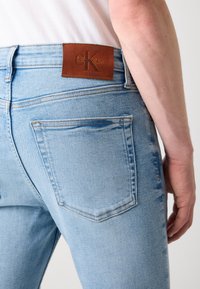 Jeans de denim azul claro con un diseño ajustado, que presentan una etiqueta de cuero marrón en la cintura y un ligero desgastado en la tela.