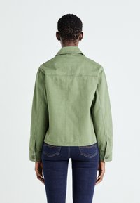 Grønn denimjakke med klassisk krage, lange ermer og knappelukking ved ermene. Baksiden har et enkelt design og en litt cropped lengde.