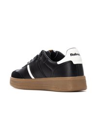Zapatilla deportiva negra con detalles perforados, raya blanca y suela de goma resistente color marrón claro. Presenta un upper de cuero suave y una pestaña en el talón de contraste.