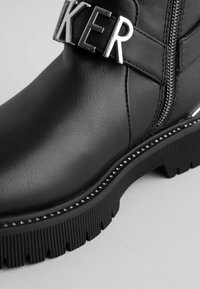 Schwarze Leder-Stiefelette mit einem dekorativen silbernen Riemen mit Buchstaben, einem seitlichen Reißverschluss und einer strukturierten Gummisohle mit Nieten.