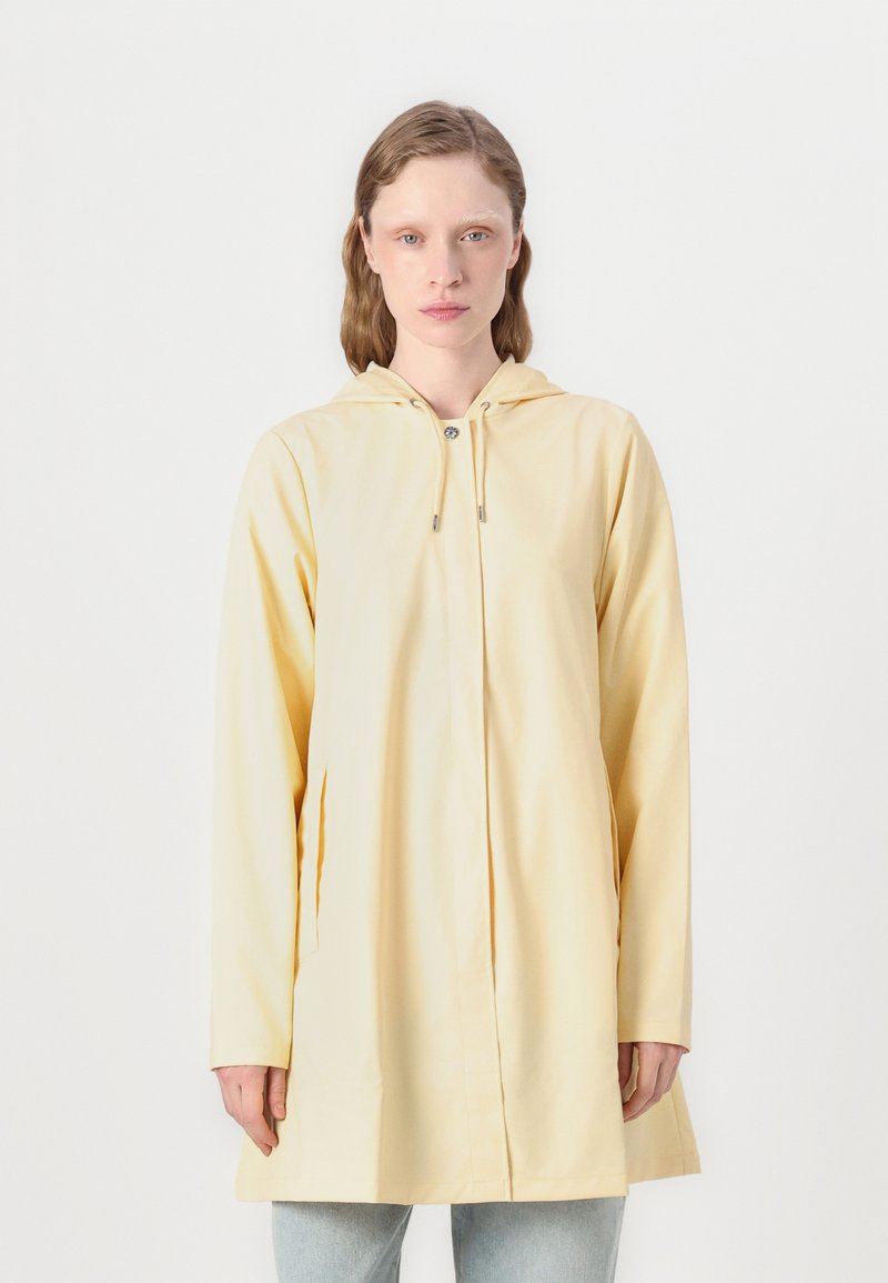 Impermeable amarillo con capucha y cremallera frontal, mangas largas y bolsillos laterales. Textura suave, de largo hasta mitad del muslo y diseño sencillo.