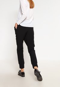 Černé úzké kalhoty s kapsami a elastickými manžetami. Kombinováno s bílým dlouhým rukávem a černými botami.