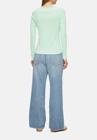 Muntgroene langemouwen top met een ronde hals, gecombineerd met wijde lichtblauwe jeans. De jeans hebben dubbele achterzakken en een rechte pasvorm.