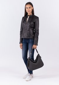 Schwarze Lederjacke mit Stehkragen, strukturierten Schultern, Reißverschluss, kombiniert mit dunklen Jeans und einer lässigen schwarzen Handtasche.