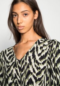 Vestido com decote em V e mangas bufantes, apresentando um padrão de pele de animal em verde e preto, feito de um tecido leve e texturizado.