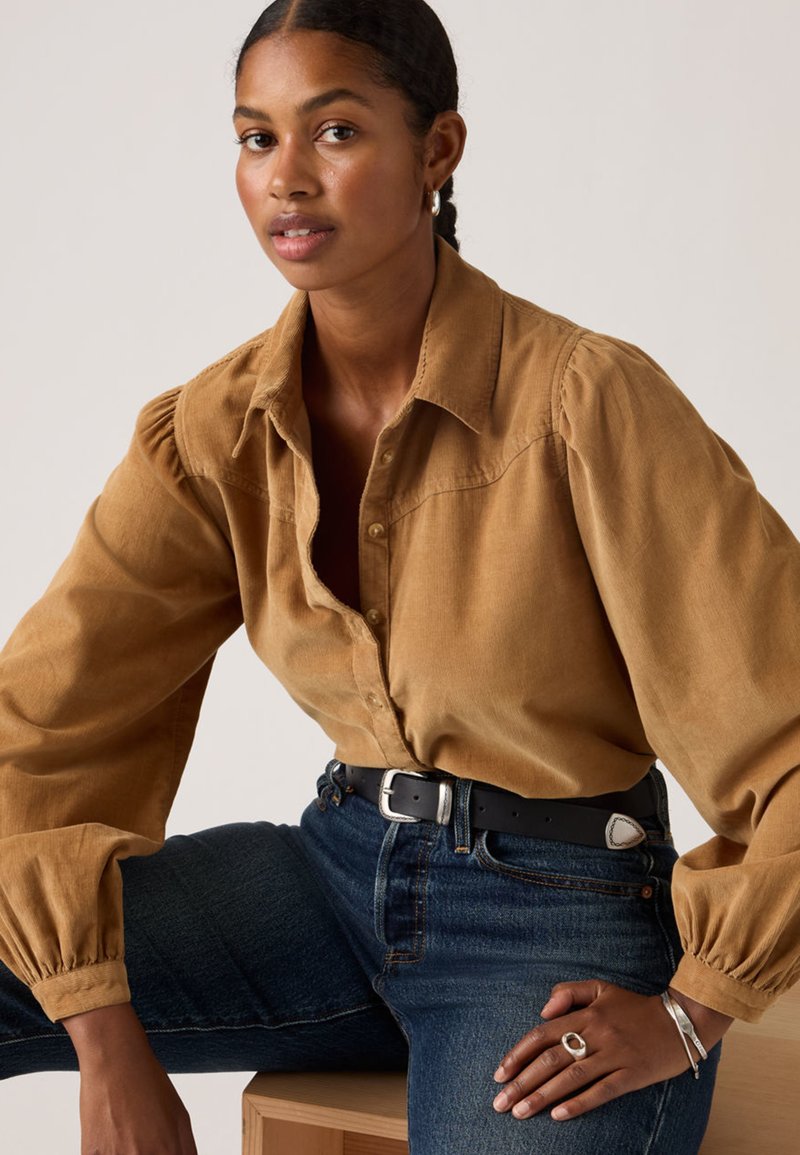 Brown corduroy button-up shirt with puff sleeves, paired with dark denim jeans and a black belt. Features silver jewelry accents.