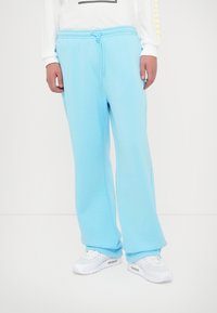 Gaiši zili sporta bikses, izgatavotas no mīkstas auduma, ar elastīgu jostu un auklu, un brīvu piegriezumu līdz potēm.