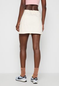 Falda corta beige con una cinturilla elástica, hecha de una tela suave. Combinada con zapatillas Nike grises y calcetines de canalé color beige.