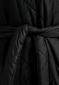 Czarna pikowana szlafrok z wiązanym paskiem, gładką fakturą i przeszyciami w romby. Materiał jest lekki i miękki.