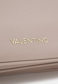 Portefeuille en cuir texturé rose clair avec un logo "VALENTINO" en or. Présente un design épuré et une finition soignée le long des bords.