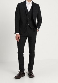 Tre-delad mörkgrå kostym med en texturerad mönster, slim-fit byxor och en vit skjorta under. Polerade mörka skor fulländar looken.