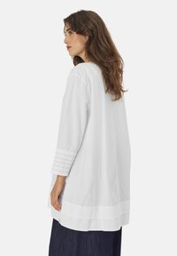 Witte, langmouw tuniek met een relaxte fit, voorzien van textuuraccenten op de manchetten en een afgeronde zoom. Lichtgewicht stof met een gladde textuur.