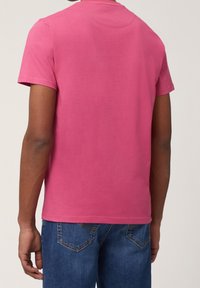 T-Shirt mit kurzen Ärmeln und Rundhalsausschnitt aus leuchtend pinkem Baumwollstoff, hat eine glatte Textur und einen schlichten Rücken, kombiniert mit blauen Denim-Jeans.