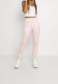 Ljusrosa, glänsande träningsbyxor med elastisk midja och muddar, kombinerat med en vit croppad topp och vita sneakers.