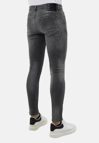 Slim-fit grijze denim jeans met een vervaagde afwerking, voorzien van een zwart logo label op de taille, en gecombineerd met witte sneakers met zwarte accenten.