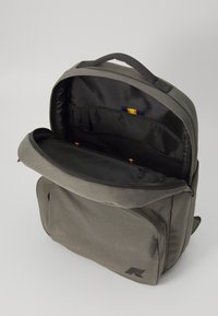Sac à dos en tissu gris avec un compartiment principal zippé, des poches intérieures et un logo noir à l'avant. Bretelles rembourrées réglables.