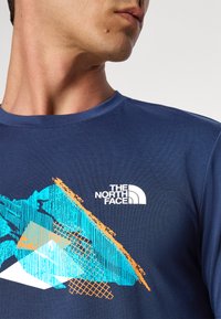 Marineblauwe T-shirt met korte mouwen van gladde stof, met kleurrijke geometrische graphics in blauw en oranje, en een wit logo op de borst.